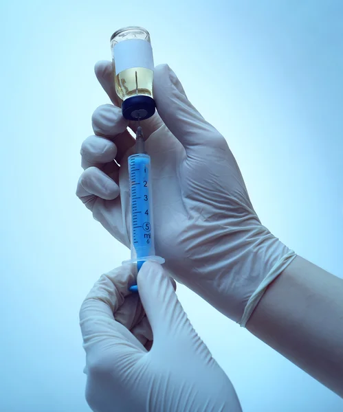 Hands in gloves filling medicine from ampule into syringe on blue background — Stock Photo, Image