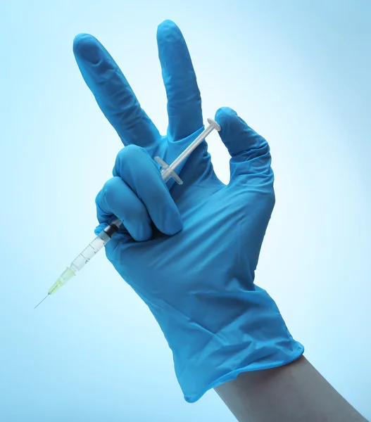 Hand in gloves with syringe on blue background — Stock Photo, Image
