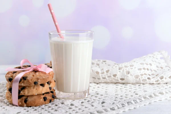 Sabrosas galletas y vaso de leche en la mesa de madera de color, sobre fondo brillante —  Fotos de Stock