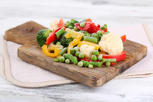 Legumes congelados na tábua de corte, no guardanapo, no fundo da mesa de madeira — Fotografia de Stock