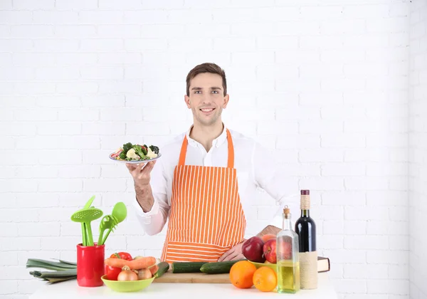 Uomo a tavola con diversi prodotti e utensili in cucina su sfondo bianco a parete — Foto Stock