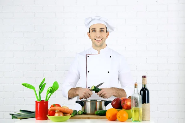 Chef at table with different products and utensil in kitchen on white wall background — Stock Photo, Image