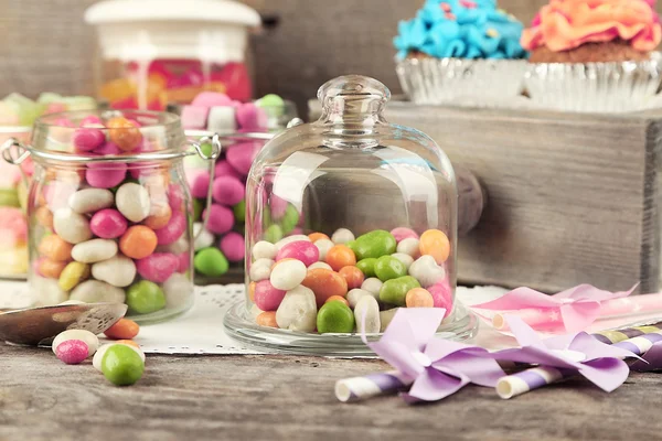 Mehrfarbige Bonbons in Glasgläsern und Cupcakes auf Holzgrund — Stockfoto