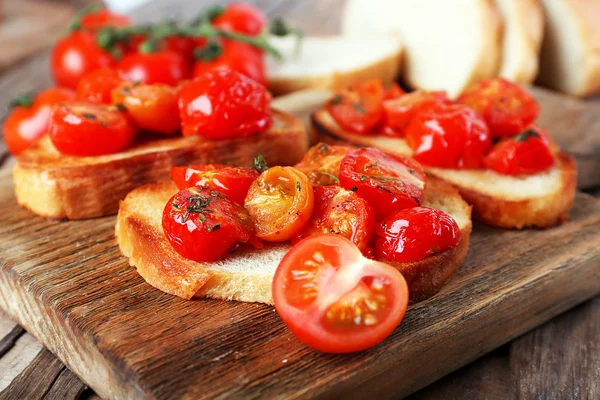 Rebanadas de pan tostado blanco con tomates enlatados en la tabla de cortar en la mesa de madera, primer plano —  Fotos de Stock