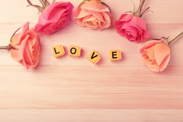 Beautiful roses with word LOVE on wooden background — Stock Photo, Image