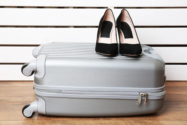 Grauer Koffer mit Frauenschuhen auf dem Boden auf weißen Planken Hintergrund — Stockfoto