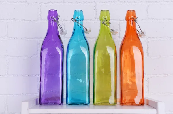 Interior design with colorful decorative glass bottles on tabletop on white brick wall background — Stock Photo, Image