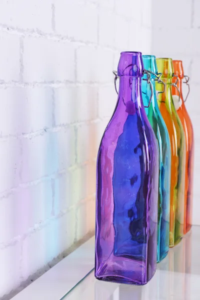 Coloridas botellas de vidrio decorativo en la mesa a lo largo de fondo de pared de ladrillo blanco —  Fotos de Stock