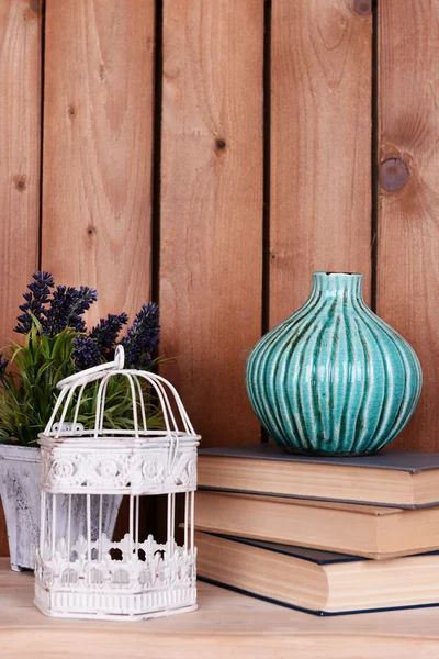 Design de interiores com vaso decorativo, gaiola, planta e pilha de livros em mesa sobre pranchas de madeira fundo — Fotografia de Stock