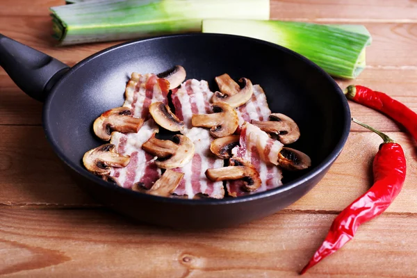 Tiras de bacon com cogumelos na panela, pimenta e chalota em pranchas de madeira fundo — Fotografia de Stock