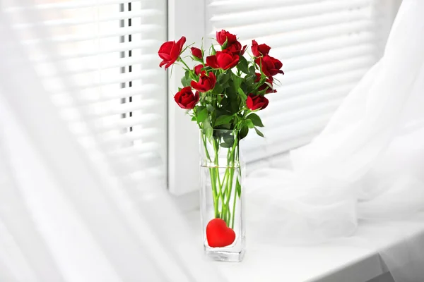Ramo de rosas rojas en jarrón de vidrio con corazón sobre fondo de alféizar de ventana —  Fotos de Stock