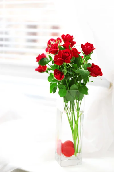 Ramo de rosas rojas en jarrón de vidrio con corazón sobre fondo de alféizar de ventana — Foto de Stock