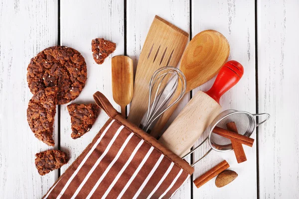 Set of kitchen utensils with cookies in mitten on wooden background — Stock Photo, Image