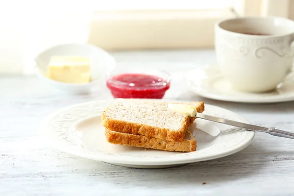 Toasts with butter on plate with cup of tea on light background — Stock Photo, Image