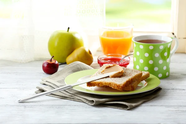 Toasts with peanut butter on plate with cup of tea and juice on light background — Stock Photo, Image