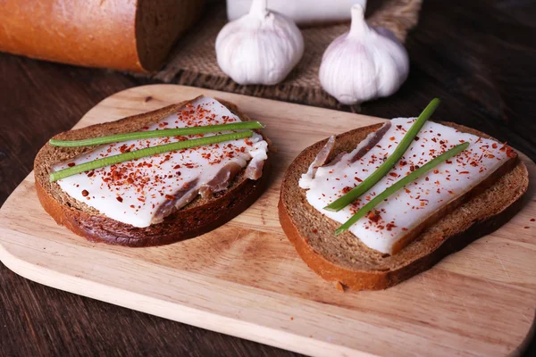 Sandwiches con manteca de cerdo en la tabla de cortar y ajo en la mesa de cerca — Foto de Stock