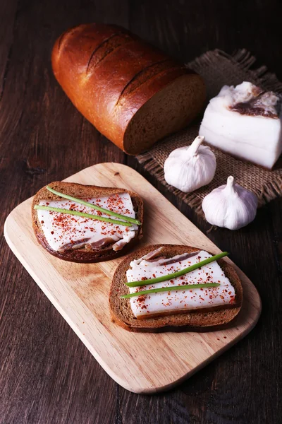 Sandwiches with lard on cutting board and garlic on wooden background — Stock Photo, Image