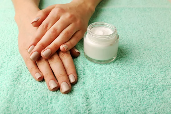 Manos femeninas con tarro de crema sobre fondo de tela — Foto de Stock