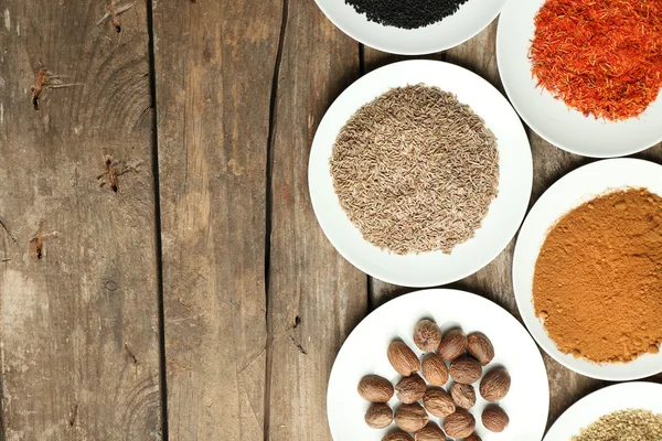 Different spices on plates, on old wooden table — Stock Photo, Image