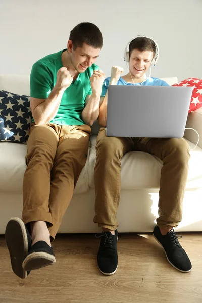 Deux beaux jeunes hommes assis sur le canapé avec ordinateur portable — Photo