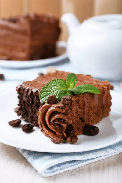 Tasty pieces of chocolate cake with mint and cinnamon on wooden table and blurred planks background — Stock Photo, Image