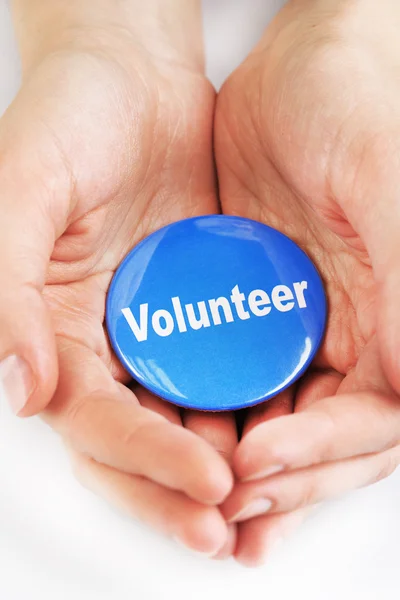 Botón de voluntario redondo en manos aisladas en blanco — Foto de Stock