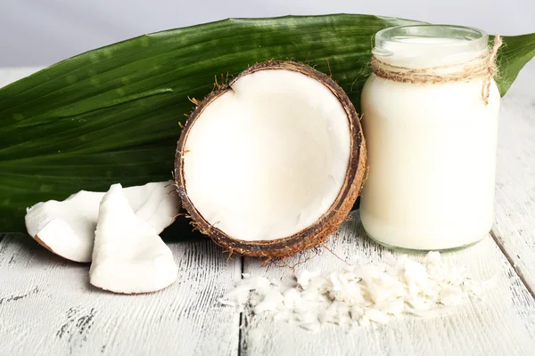 Óleo de coco fresco em garrafa de vidro e folha verde na cor de fundo de mesa de madeira — Fotografia de Stock