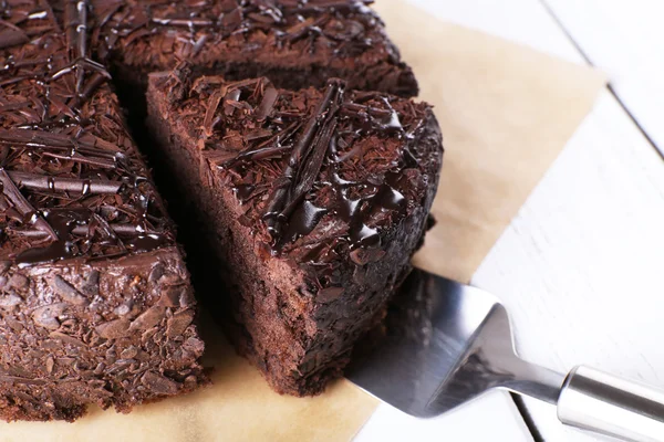 Bolo de chocolate saboroso fatiado em folha de pergaminho na mesa de madeira, close-up — Fotografia de Stock