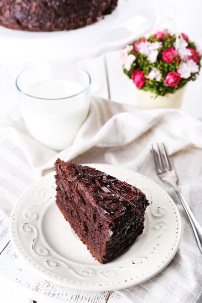 Нарезанный вкусный шоколадный торт на тарелке и стакан молока на столе, крупным планом — стоковое фото