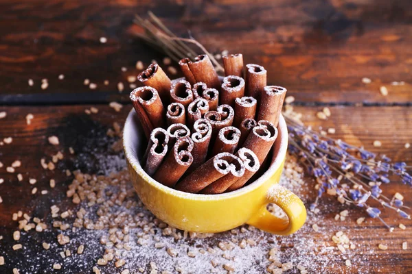 Palitos de canela en taza con azúcar y lavanda sobre fondo de mesa de madera — Foto de Stock