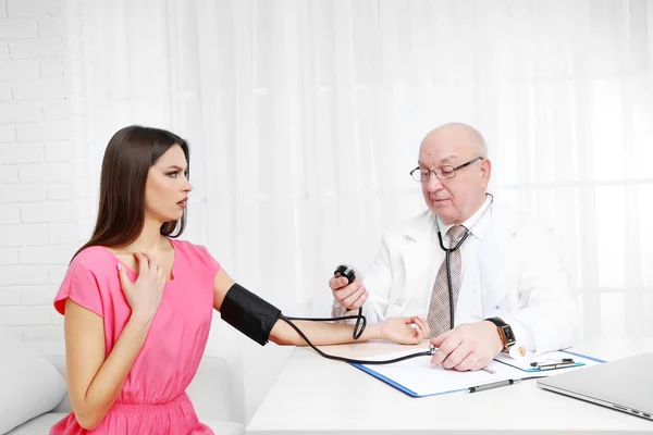 Médecin professionnel mesurant la pression artérielle dans son bureau sur fond de rideau blanc — Photo