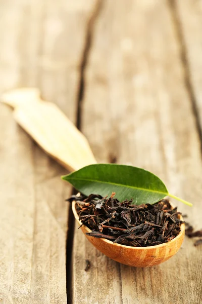 Svart te med blad i sked på gamla träbord — Stockfoto