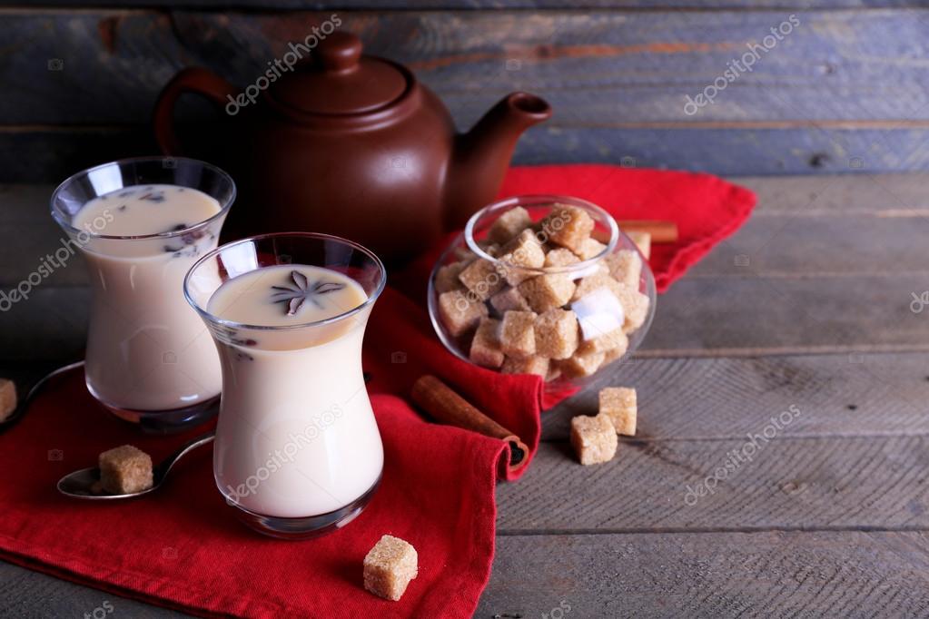 Black tea with milk in glasses and teapot with lump sugar on color
