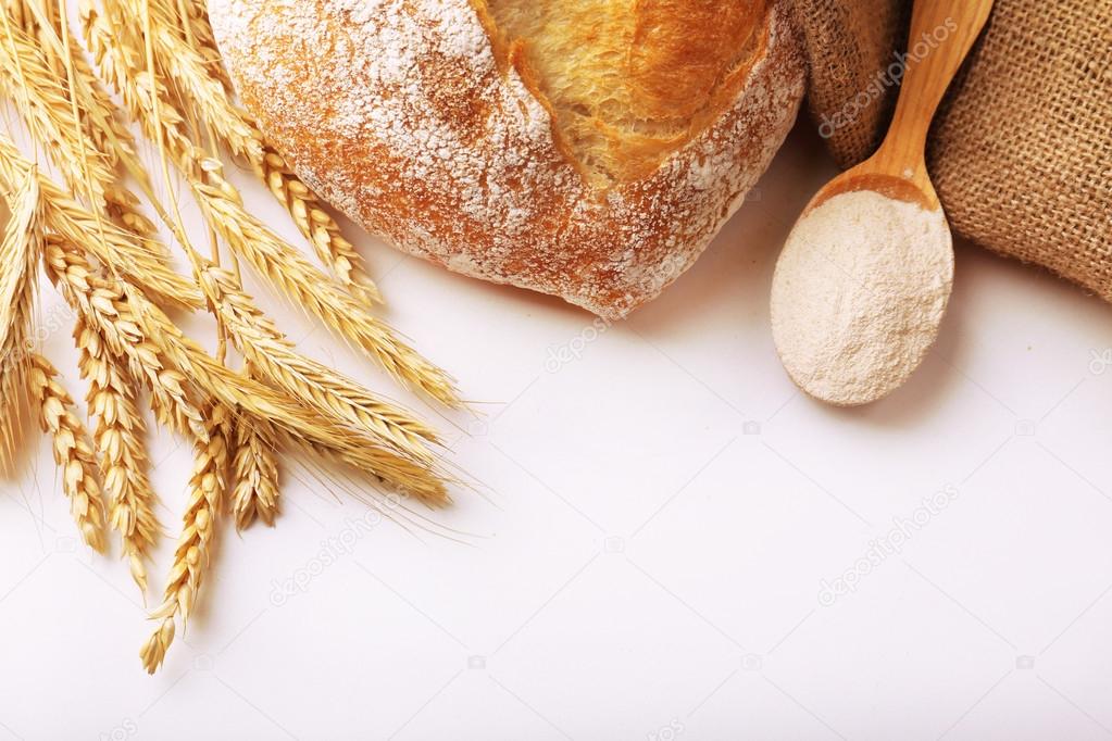Fresh bread with wheat and wooden spoon of flour isolated on white
