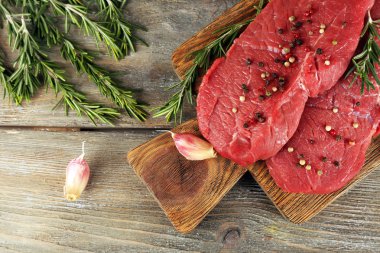 Raw beef steak with rosemary and garlic on cutting board on wooden background clipart