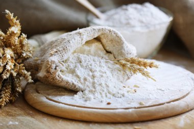 Flour in burlap bag on cutting board and wooden table background clipart