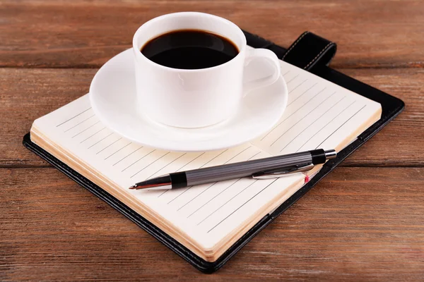 Taza de café en platillo con diario y pluma sobre fondo de mesa de madera — Foto de Stock