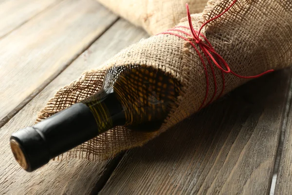 Wijnfles verpakt in jute doek op houten planken achtergrond — Stockfoto