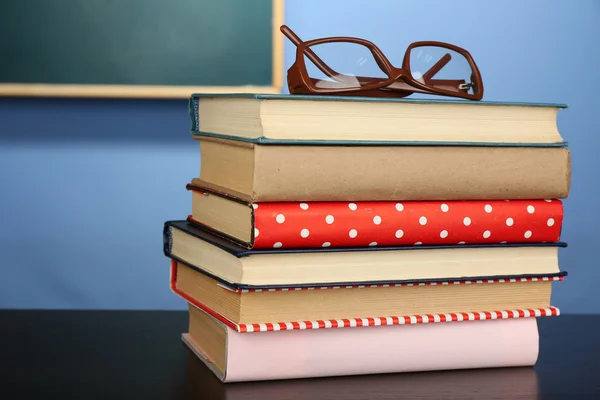 Pilha de livros com óculos na mesa de madeira, na parede colorida e no fundo do quadro negro — Fotografia de Stock