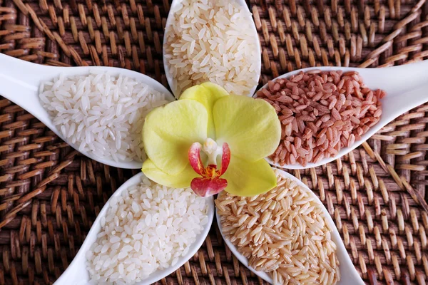 Diferentes tipos de arroz en cucharas sobre fondo de mimbre — Foto de Stock