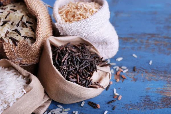 Diferentes tipos de arroz em sacos no fundo de madeira — Fotografia de Stock