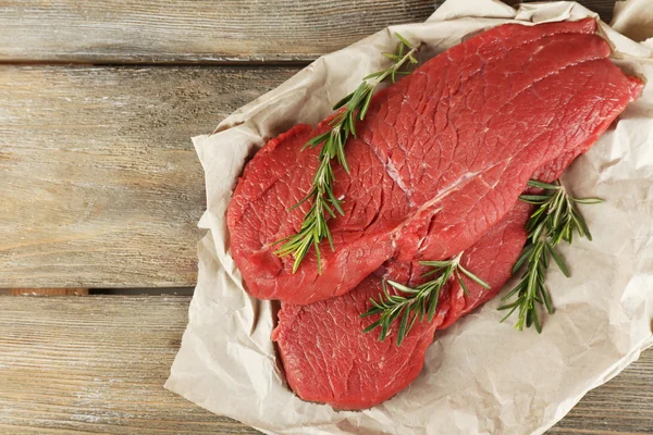 Raw beef steak with rosemary on paper on wooden background — Stock Photo, Image