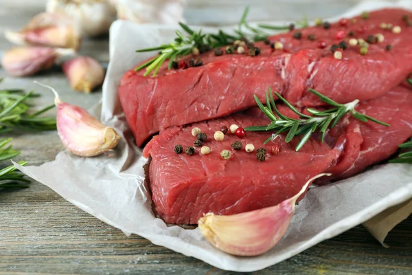 Raw beef steak with rosemary and garlic on paper on wooden background — Stock Photo, Image