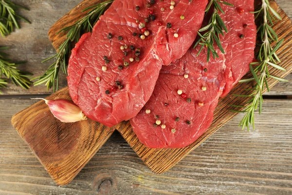 Rauwe biefstuk met rozemarijn en knoflook op snijplank op houten achtergrond — Stockfoto