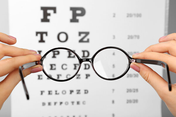 Glasses in hands on eye chart background, close-up