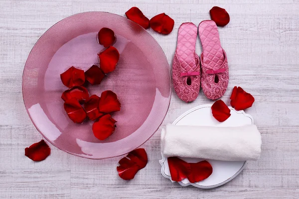 Wellnessschale mit Wasser, Rosenblättern, Handtuch und Hausschuhen auf hellem Hintergrund. Konzept der Pediküre oder natürlichen Wellness-Behandlung — Stockfoto