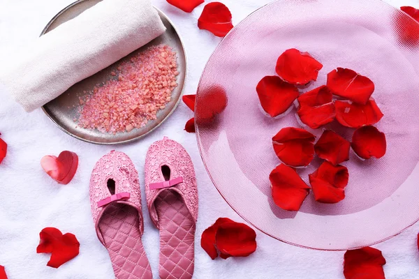 Spa bowl with water, rose petals, towel and slippers on light background. Concept of pedicure or natural spa treatment — Stock Photo, Image