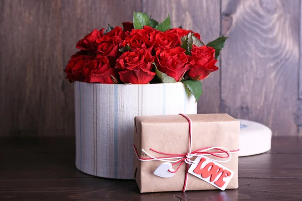 Strauß roter Rosen in Textilbox mit Geschenk auf Holzgrund — Stockfoto