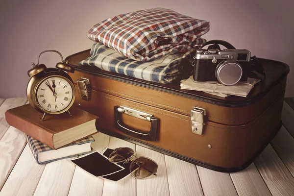 Mala vintage com roupas e livros na mesa sobre fundo colorido escuro — Fotografia de Stock