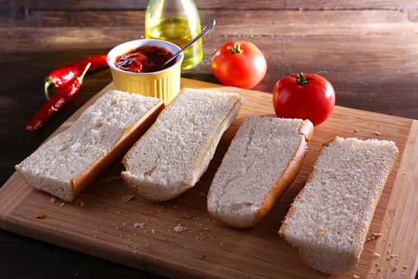 Slices of bread with tomato sauce on cutting board on wooden background — Stock Photo, Image